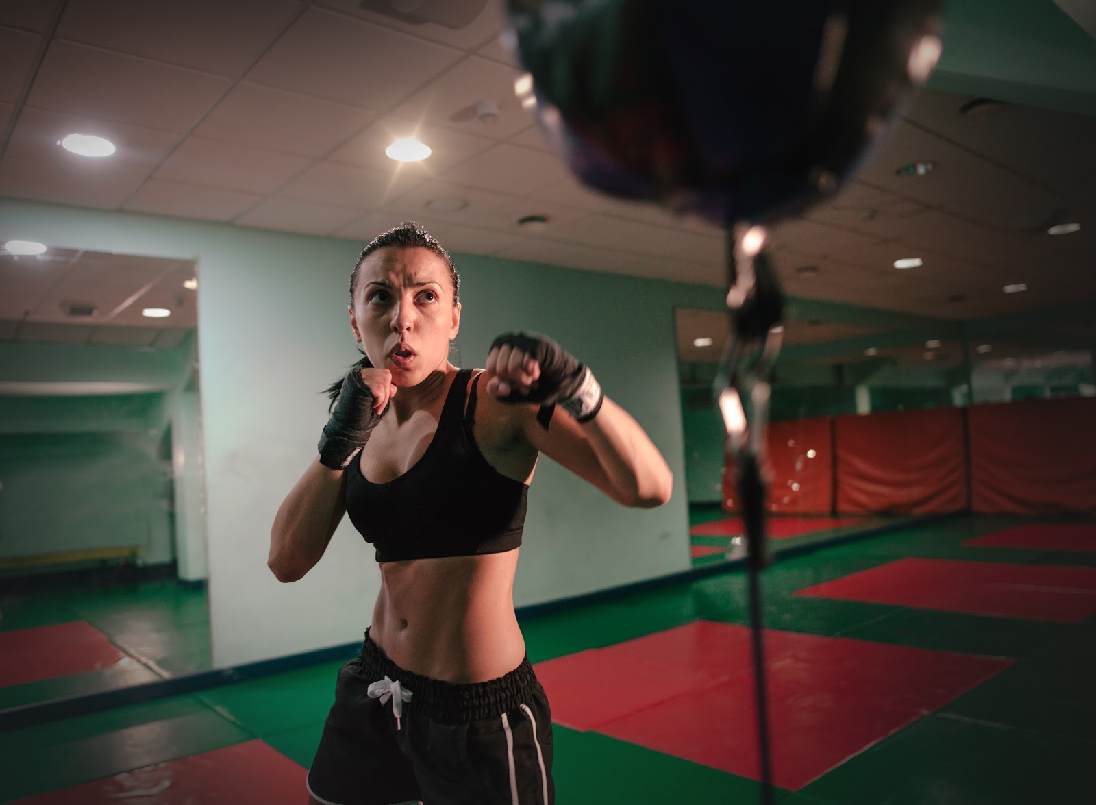 Female brunette boxer with hair and black gym wear and black hand-wraps punching a double-ended boxing bag.