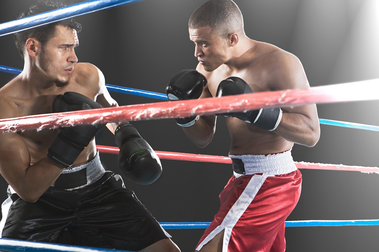 Two boxers in action in the ring, on one on the defensive and the other attacking.