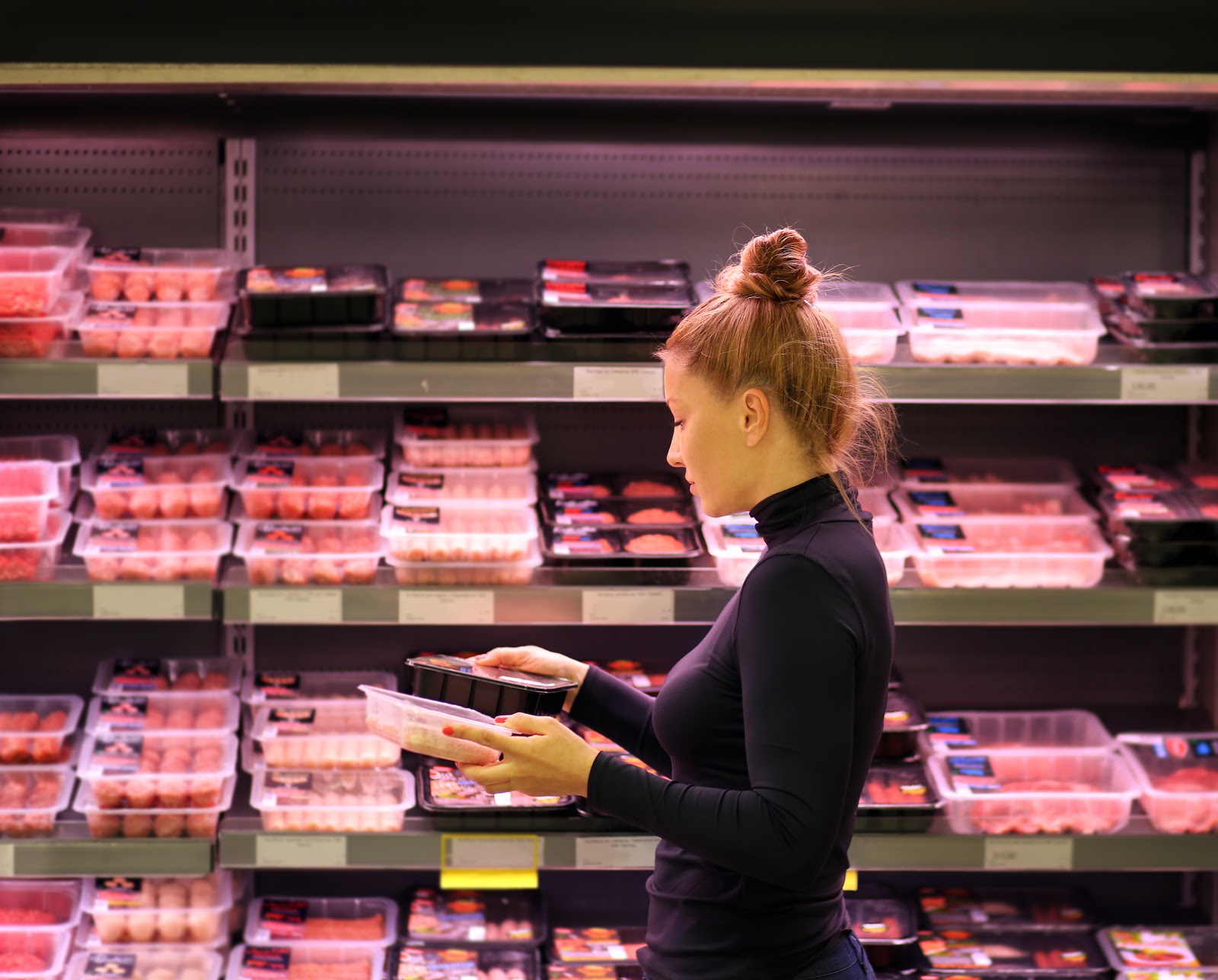 Woman choosing meat in supermarket aisle. 